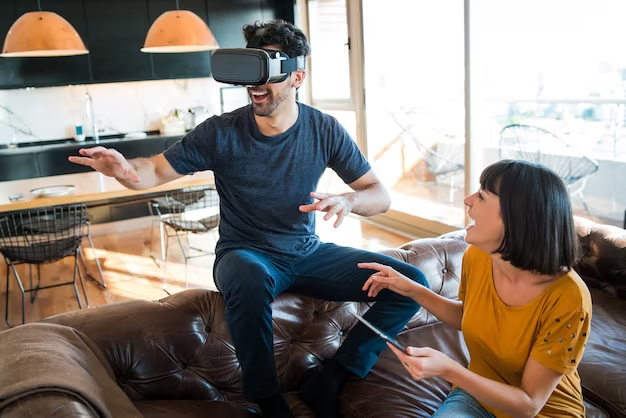 A man wearing a VR headset playing alongside a woman laughing while watching him.